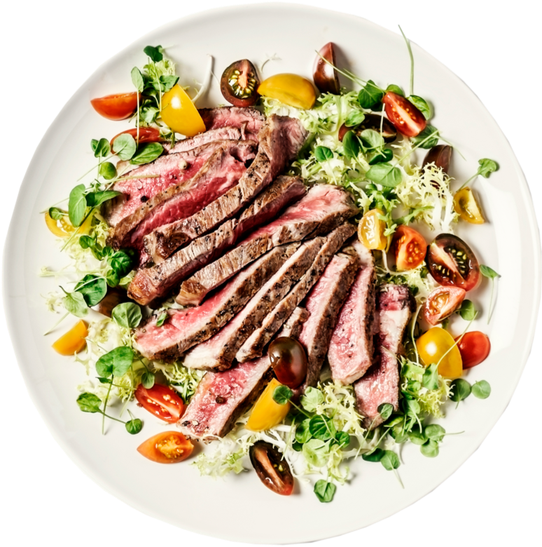 Sliced steak salad plated with cherry tomatoes, greens and fresh herbs