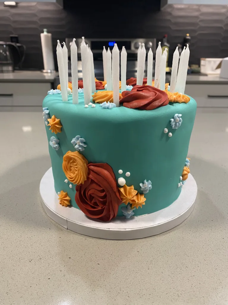 Teal fondant celebration cake decorated with red roses and lit candles