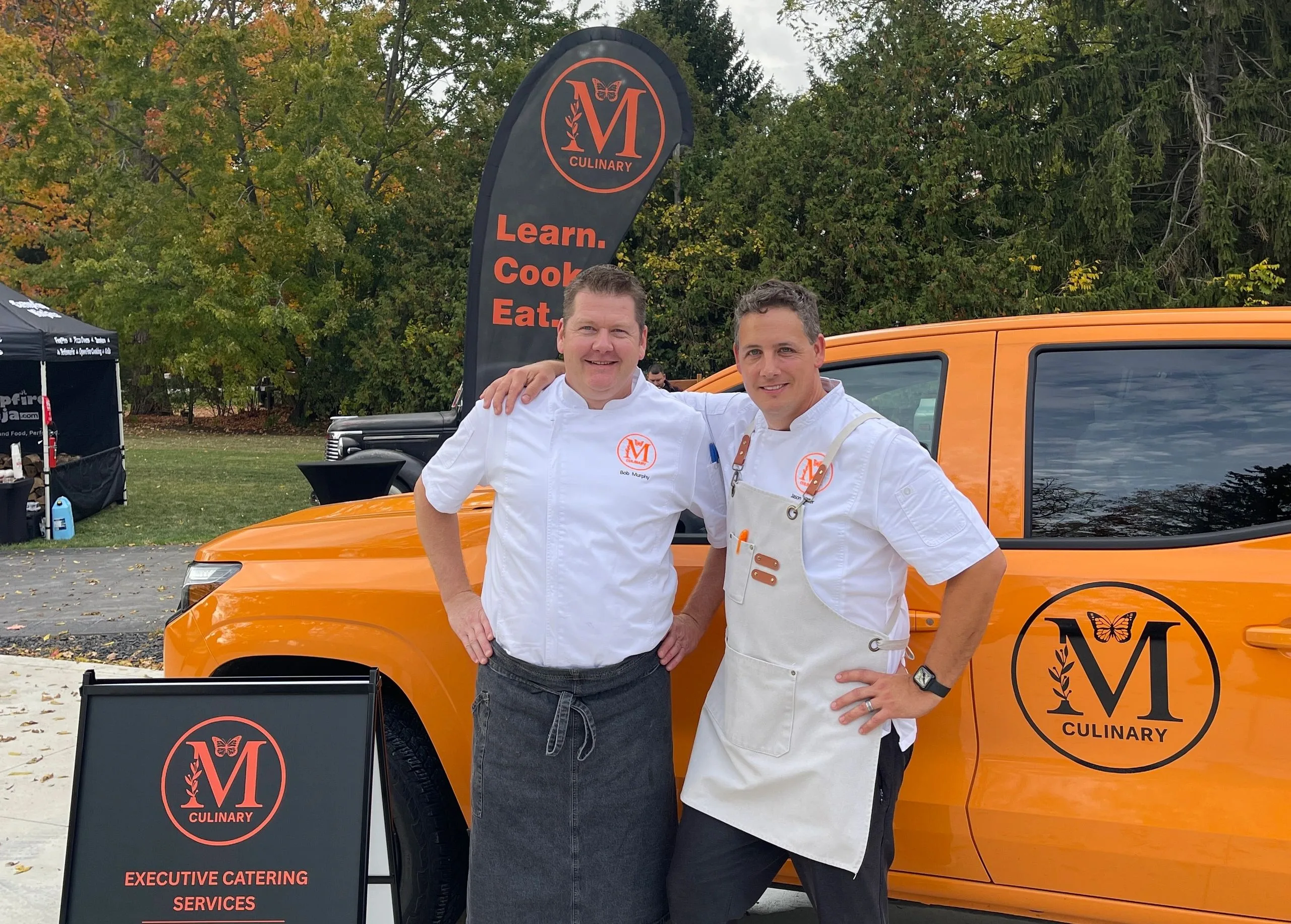 The Monarch Culinary chefs in front of their orange catering van with the Learn. Cook. Eat. banner