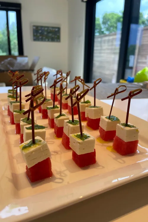 Watermelon and feta skewers with herb drizzle, served as a fresh summer appetizer on a white platter
