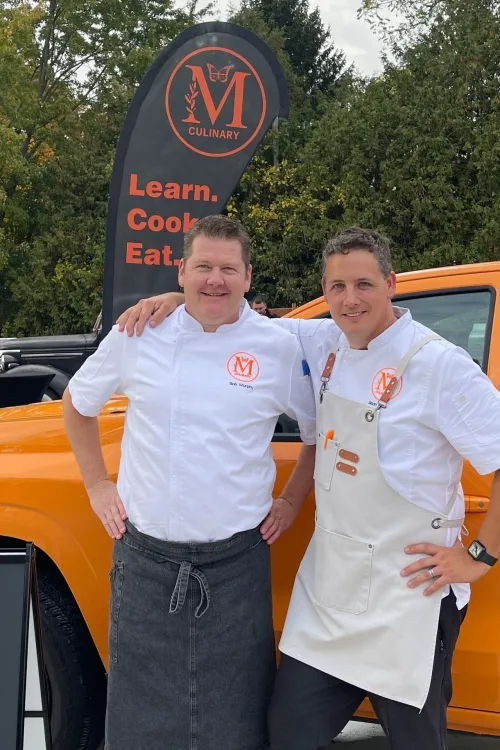 The Monarch Culinary chefs in front of their orange catering van with the Learn. Cook. Eat. banner